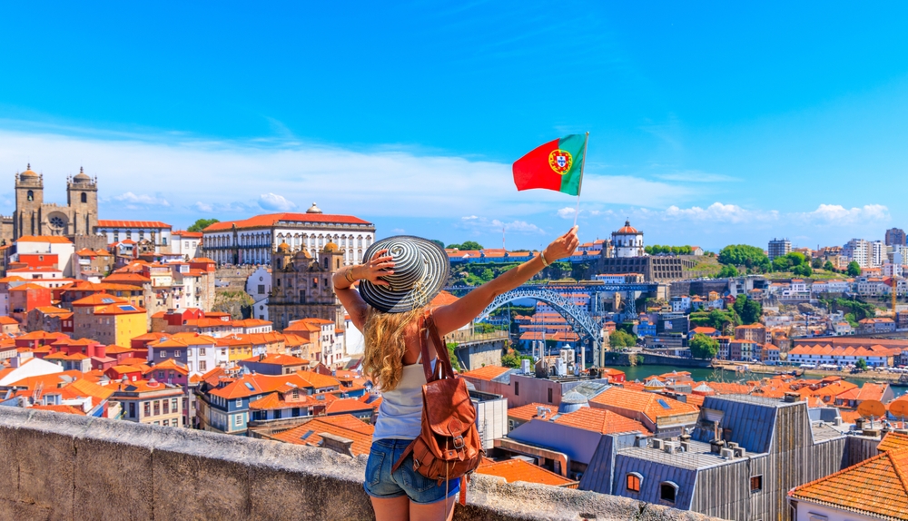 Traveller overlooking Porto cityscape, holding Portuguese flag with Dom Luís I Bridge and rooftops in view
