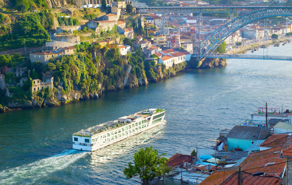 A white cruise ship sailing on the Douro River in Porto under the Dom Luis I Bridge