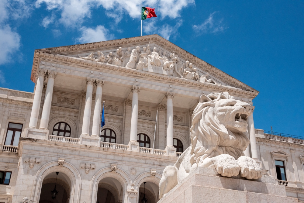 Neoclassical Portuguese Parliament building with lion statue and flag under bright blue Lisbon sky
