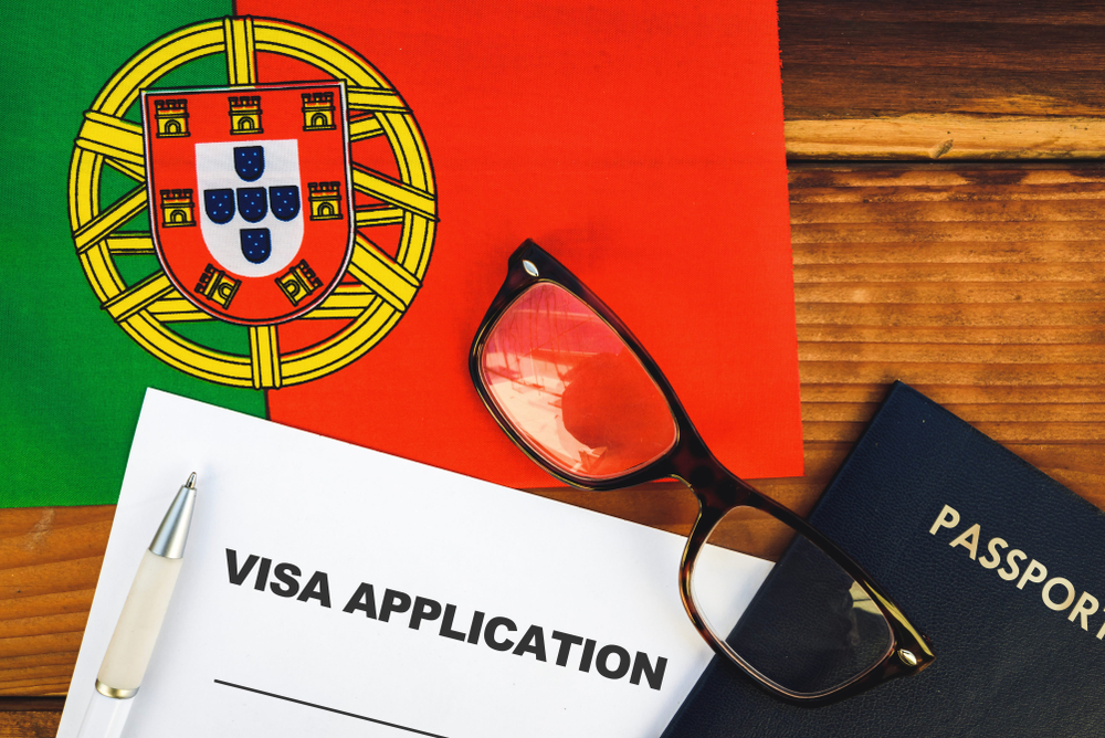 Pen and reading glasses resting on a visa application form and passport and Portuguese flag