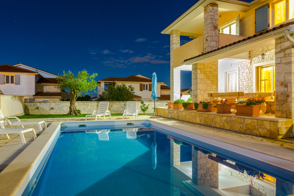 Stone villa with an illuminated swimming pool and white lounge chairs at night