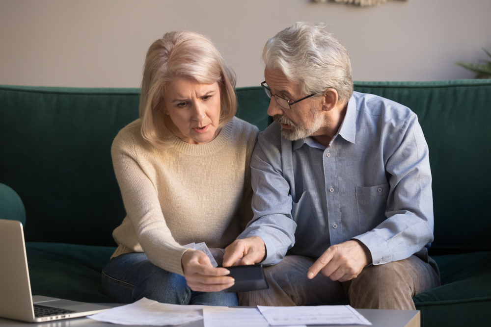 Concerned senior couple reviewing financial documents and a calculator on a sofa