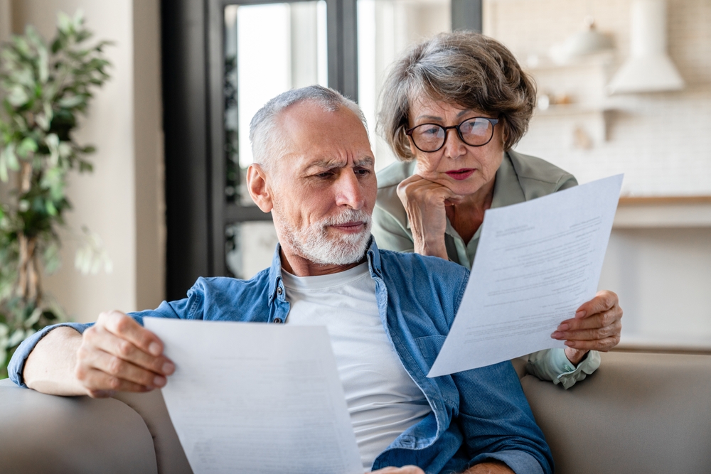 Senior couple looking worried reviewing bills and financial documents at home