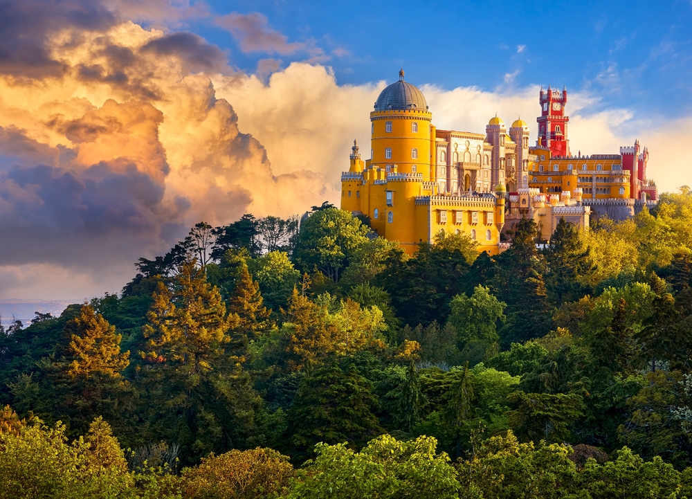 The colorful Pena Palace in Sintra on a hilltop surrounded by a lush green forest at sunset
