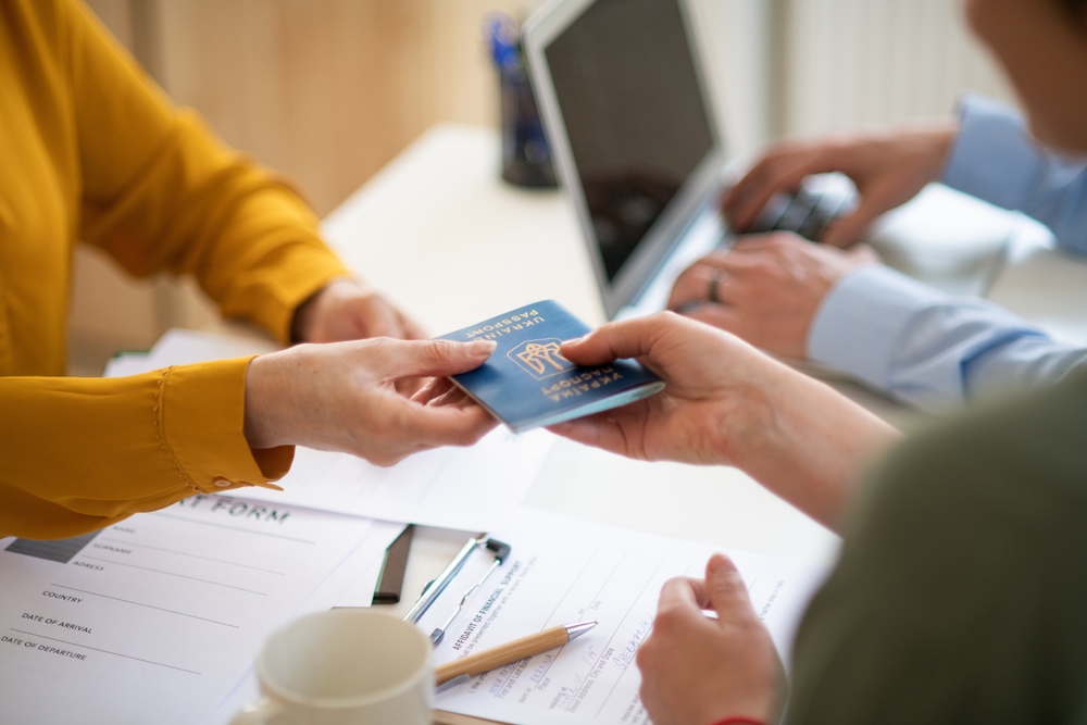 Hands exchanging a Ukrainian biometric passport over a form during a visa or immigration application process