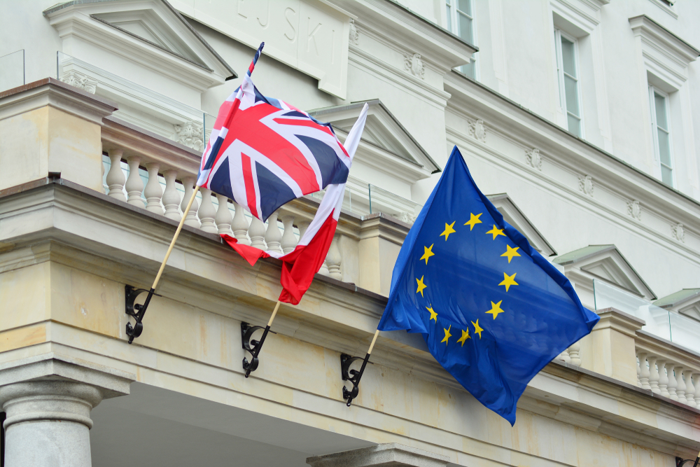 British and European Union flags flying from the balcony of a white classical building