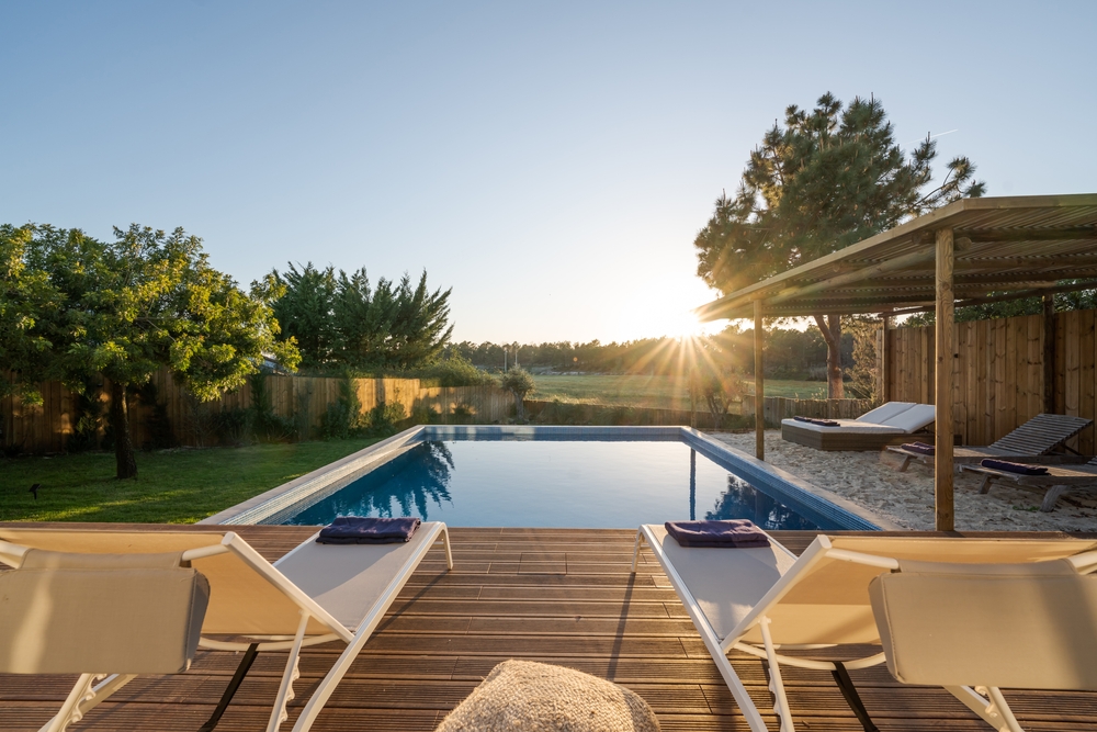Back garden swimming pool with lounge chairs on wood deck at sunset