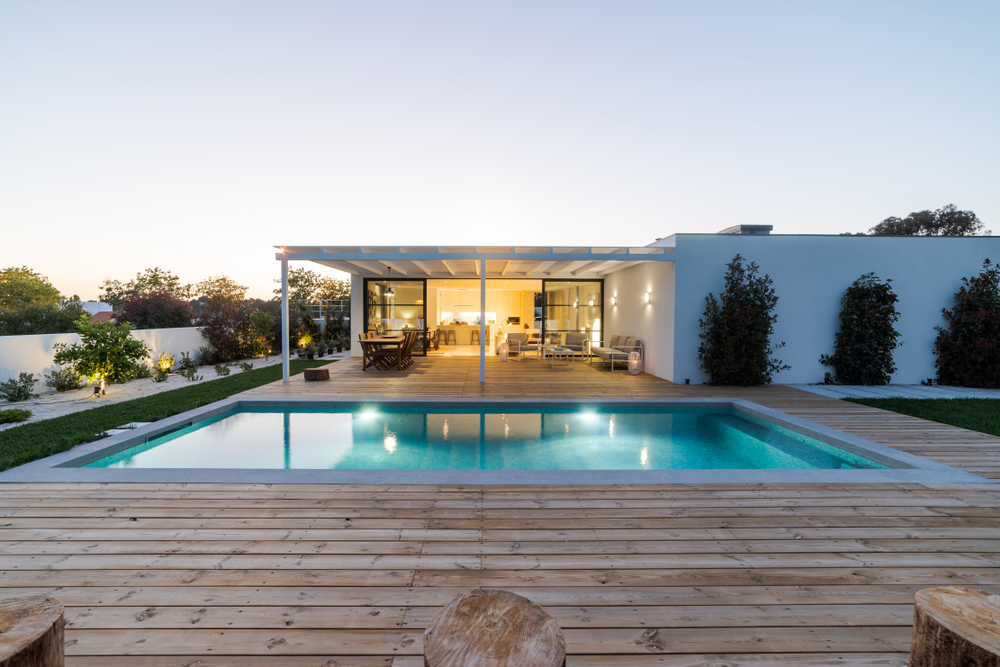 Modern villa with an illuminated swimming pool and large wooden deck at twilight