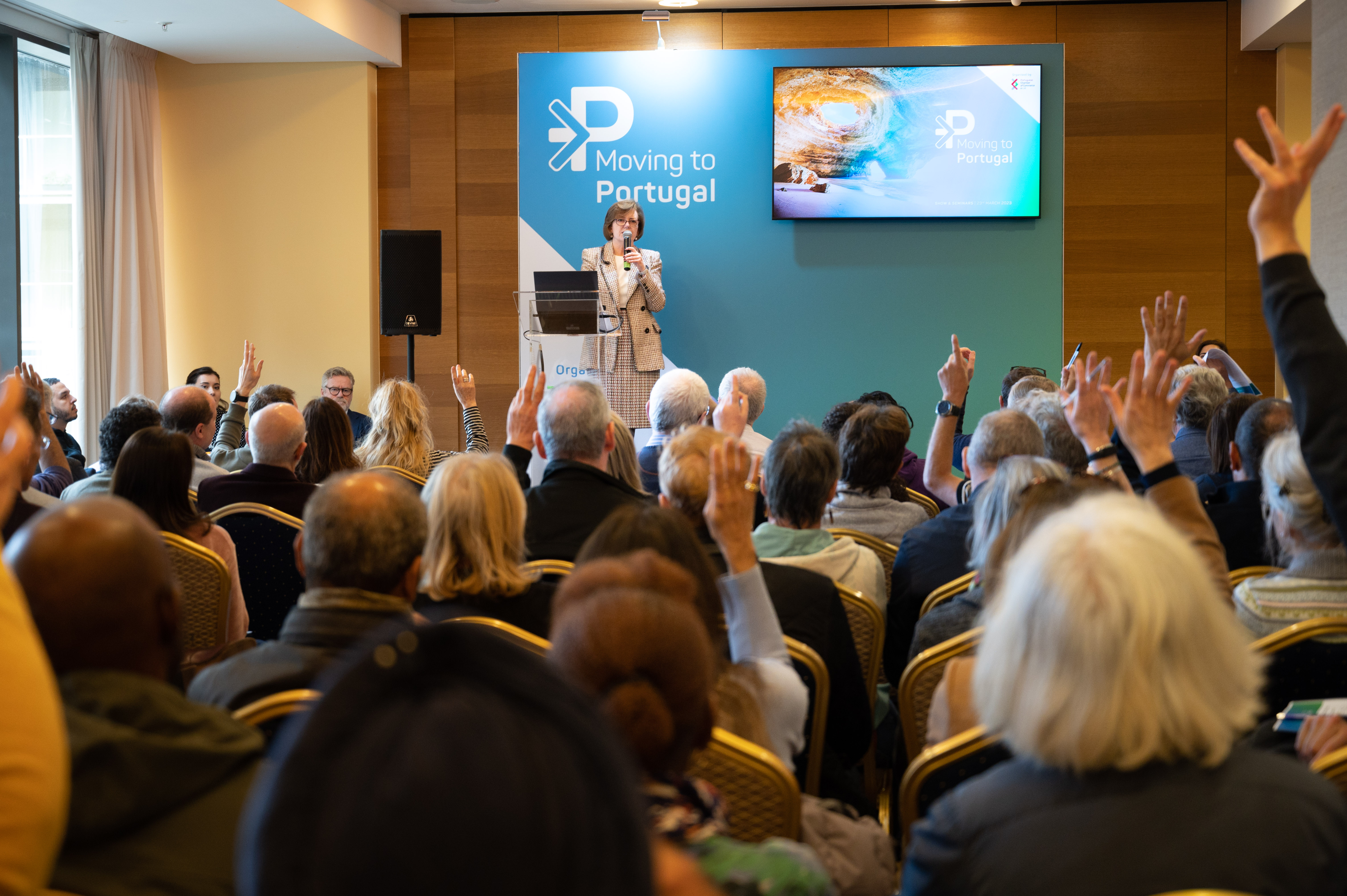 A speaker presenting at the 'Moving to Portugal' seminar to a large, engaged audience