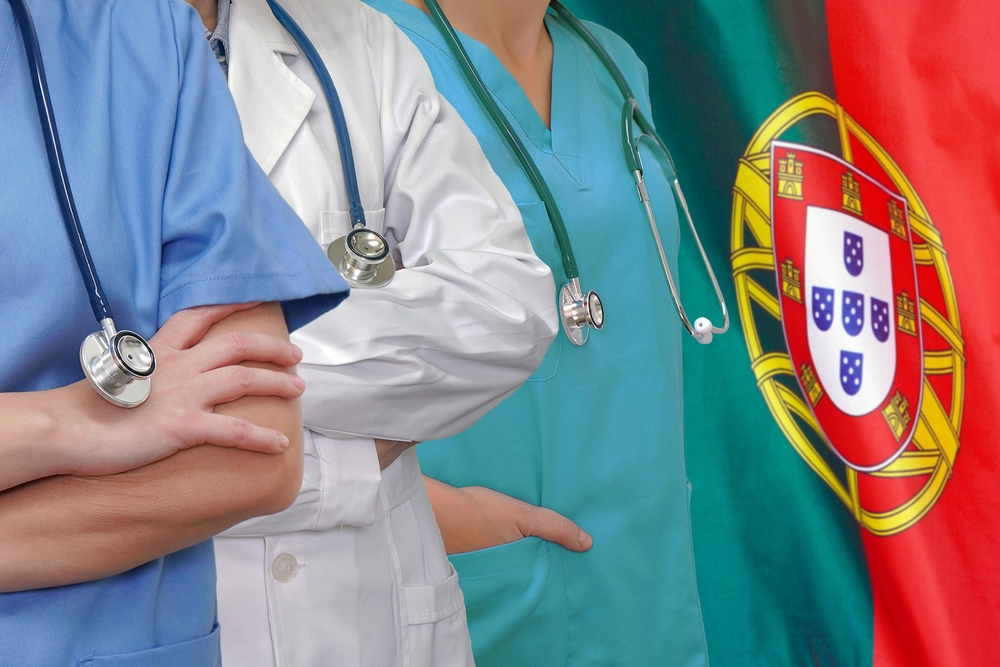 Three healthcare workers in scrubs and lab coats with stethoscopes by a Portugal flag