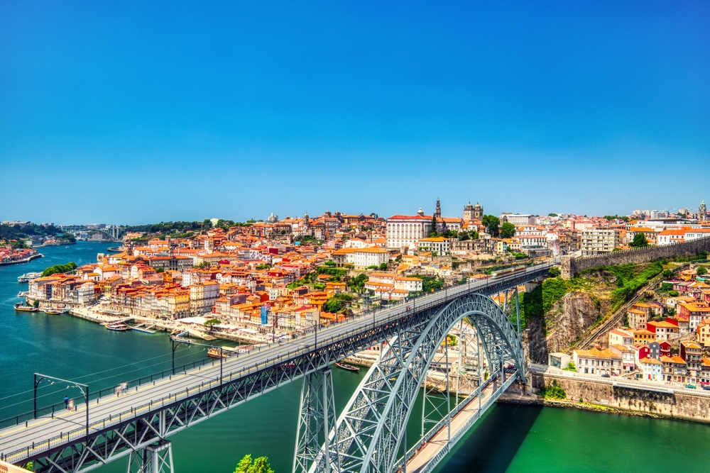 Dom Luís I Bridge and historic Porto city skyline along the Douro River under bright blue skies