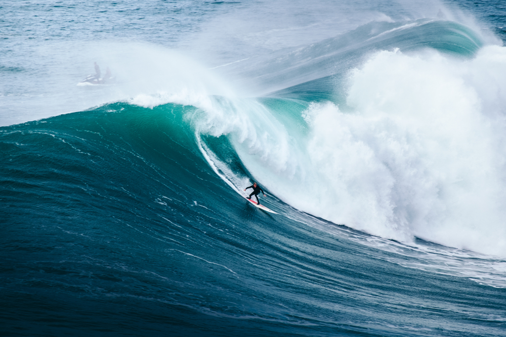 Solo surfer skillfully riding a gigantic powerful blue ocean wave at Nazaré in Portugal