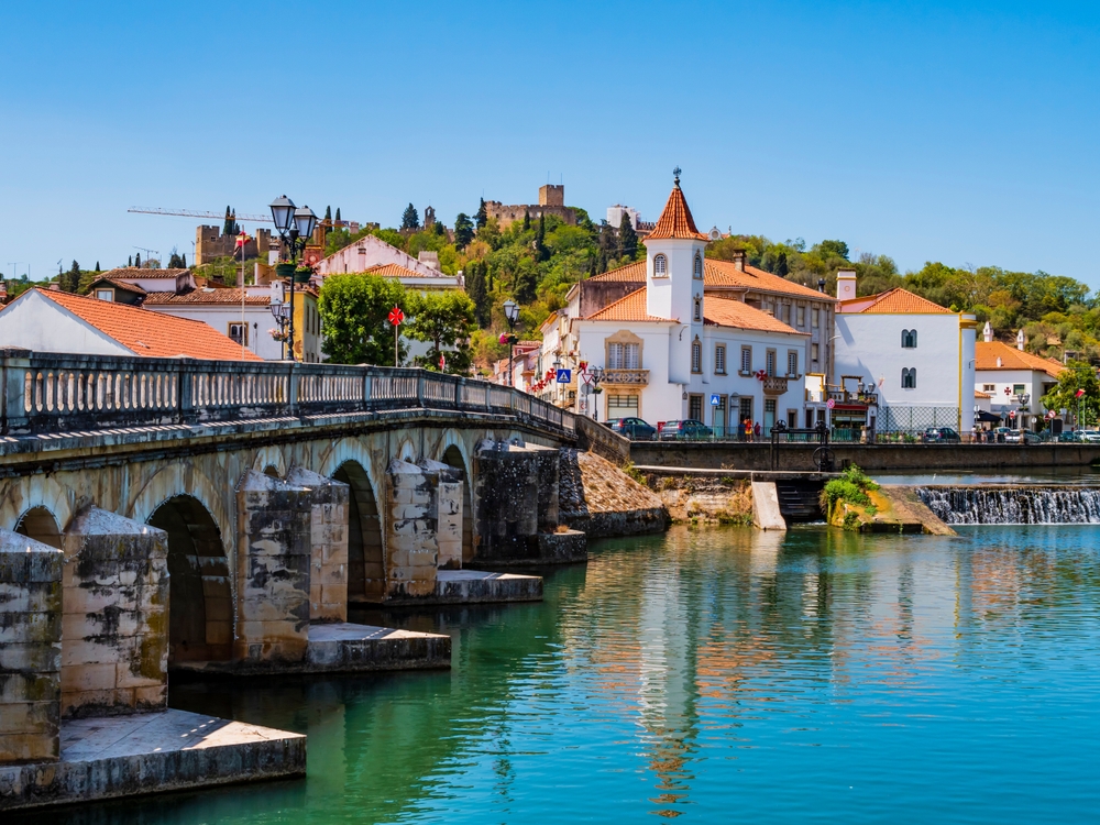 Sunlit view of the Ponte Velha bridge and white buildings along the Nabão River in Tomar