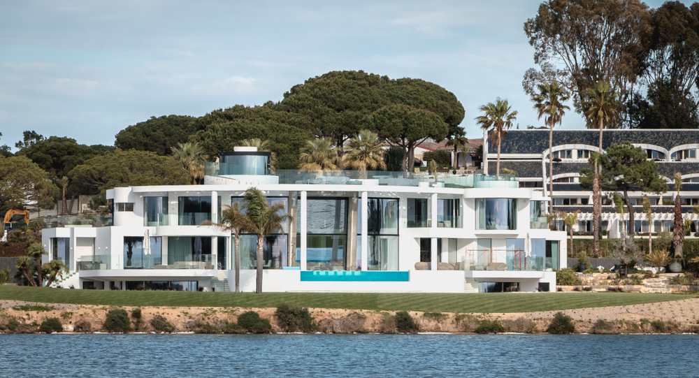 Circular white luxury villa with glass walls and an infinity pool facing the water