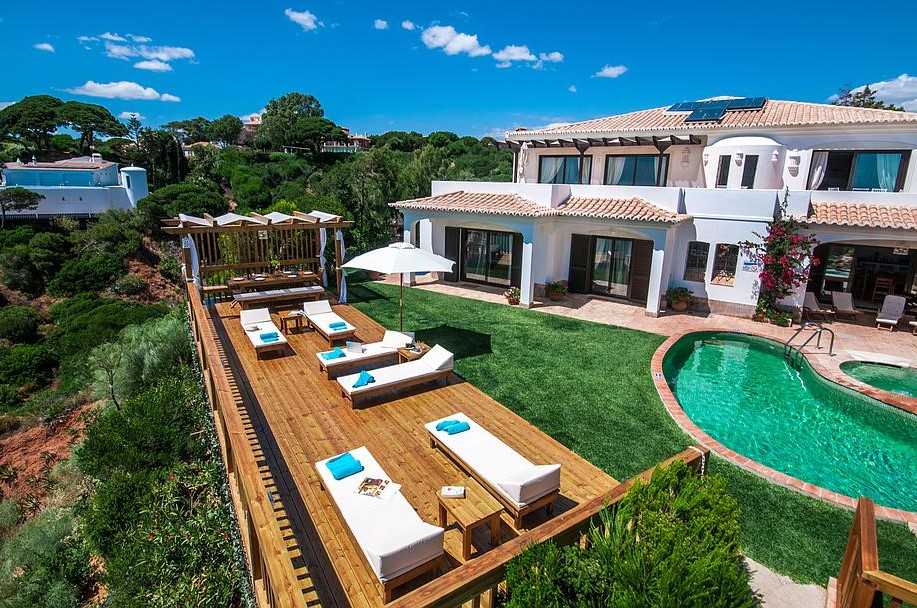 Luxury villa with a pool, lawn and deck featuring lounge chairs on a sunny day