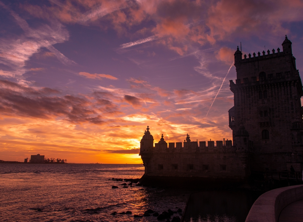 Silhouetted stone architecture of Belem Tower in Lisbon against a vibrant orange and purple sunset