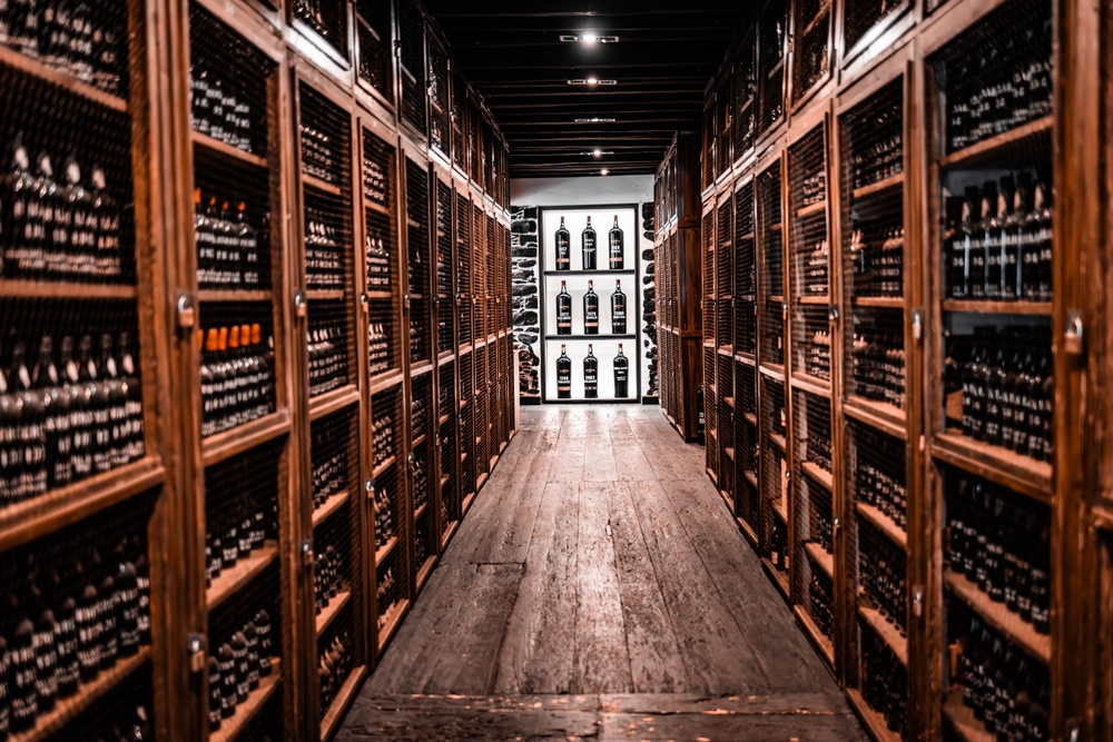 A long hallway in a wine cellar lined with tall wooden racks filled with vintage bottles