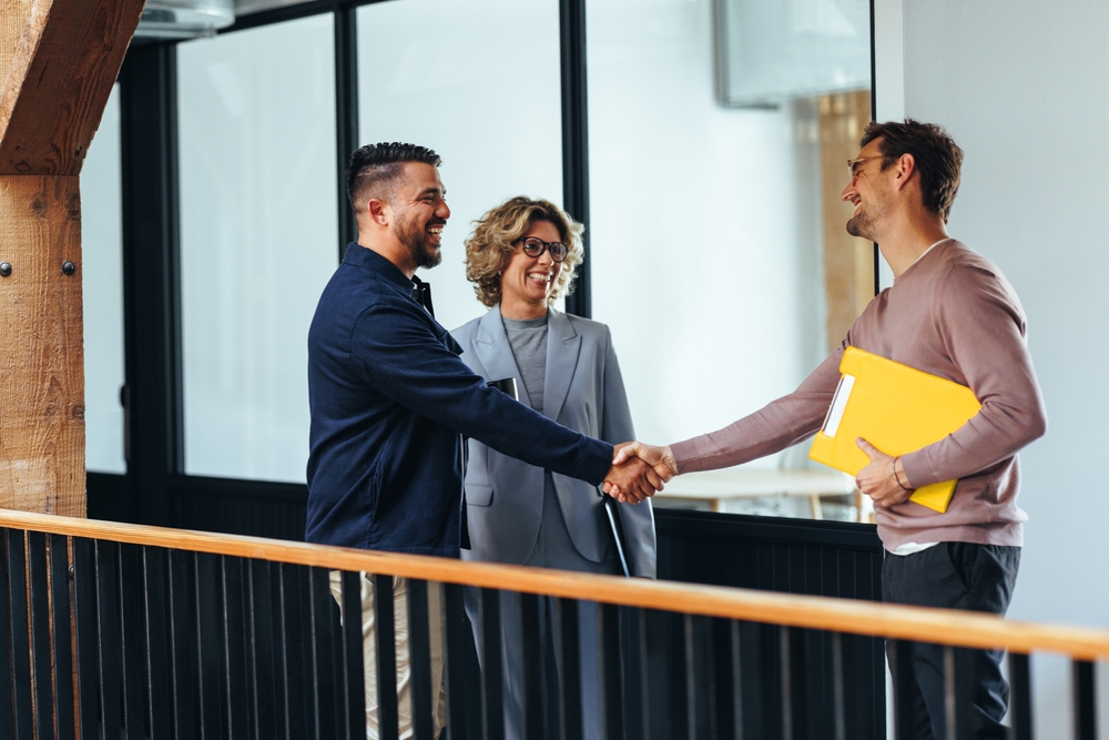 Three people in an office shaking hands and smiling, suggesting a successful business meeting