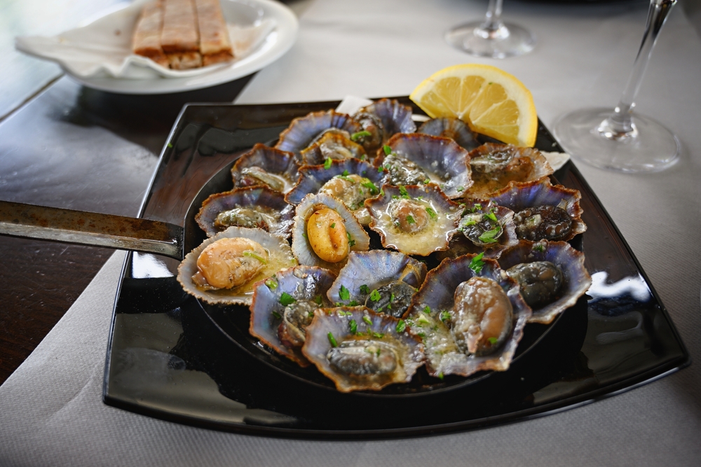 Portuguese dish of grilled limpets with parsley and lemon on served on a black plate 