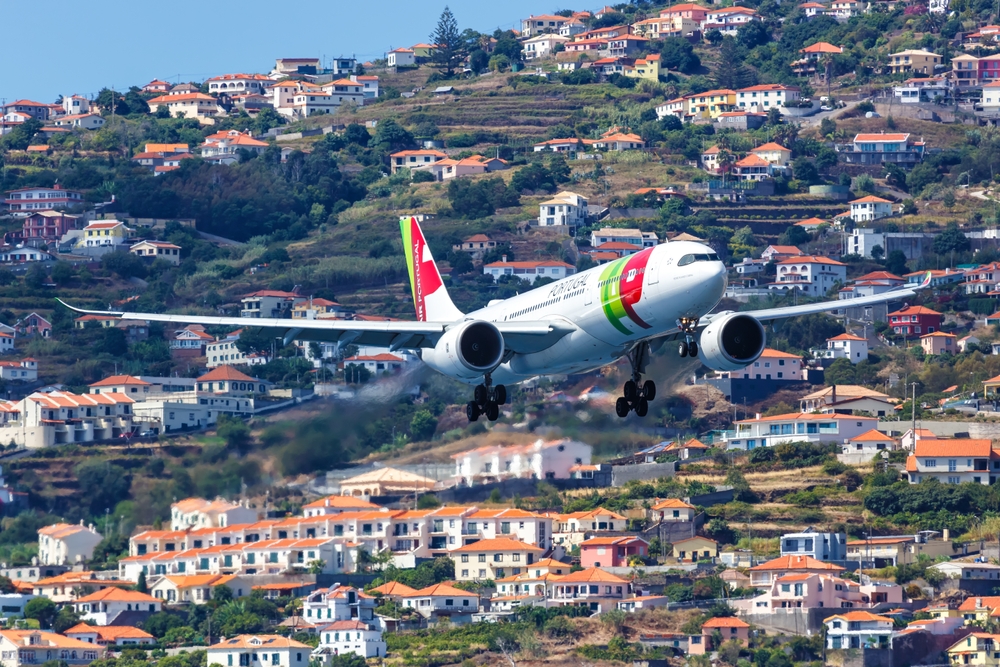 TAP Air Portugal wide-body airplane flying low over a densely populated hillside