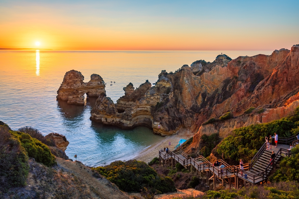 Wooden boardwalk leading to a beach with golden cliffs and a sunset over the Atlantic
