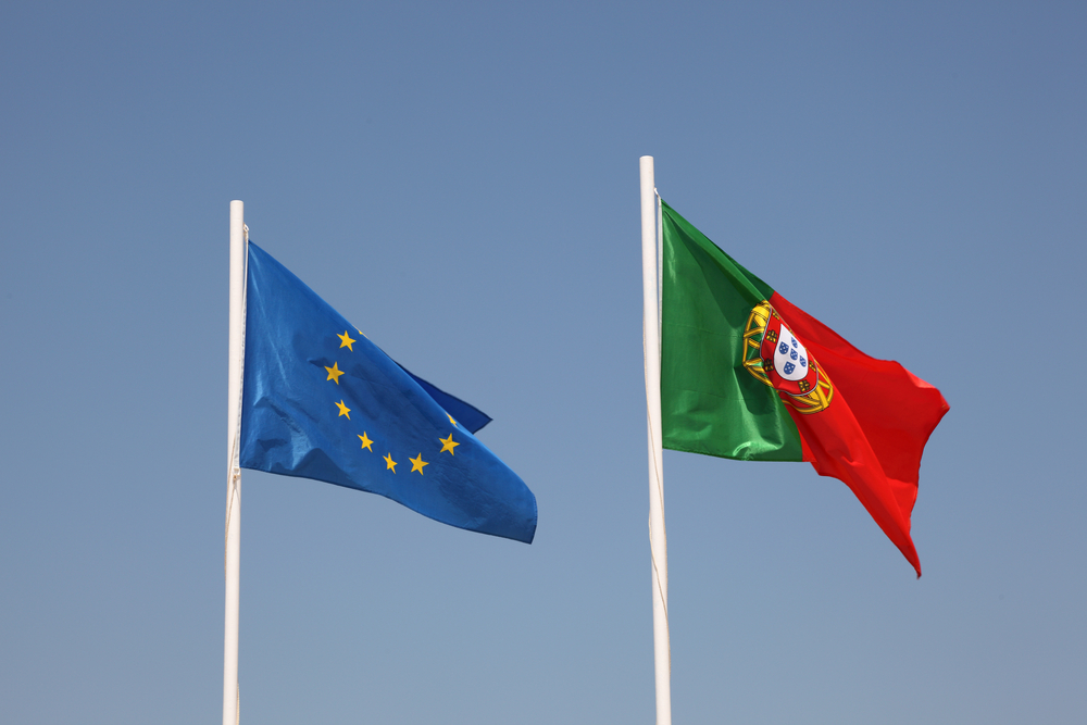 National flags of the European Union and Portugal flying on white poles against a blue sky