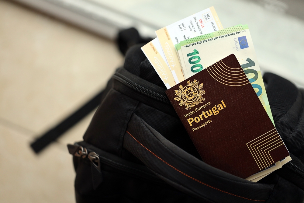 A Portuguese passport, boarding passes, and Euro banknotes tuck into a black travel backpack
