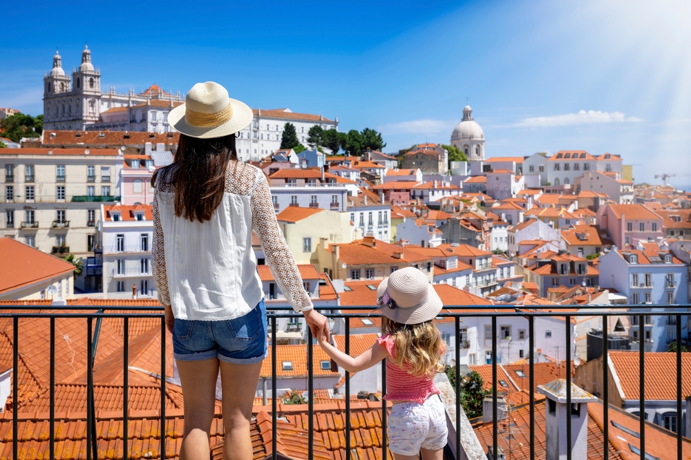 A mother and child in sun hats overlooking Lisbon's red-roofed buildings and the river