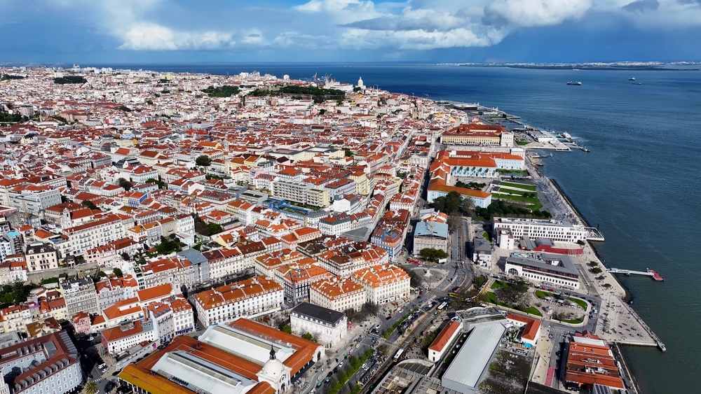 Aerial view of Lisbon's red-roofed buildings and the Tagus River under a cloudy sky