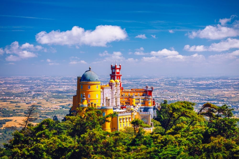 Vibrant yellow and red Pena Palace on a lush hilltop in Sintra, Portugal, under blue sky