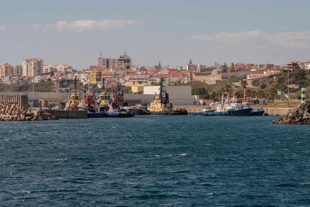 Industrial tugboats docked in a harbour with coastal town of Sines in the background