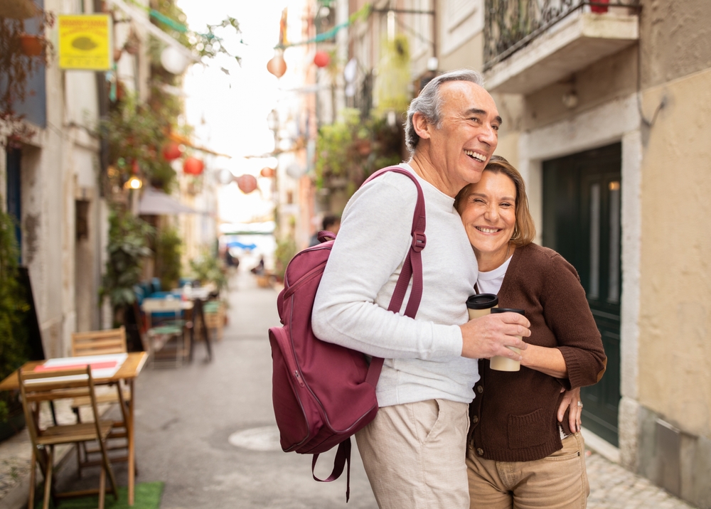 Smiling older couple hugging in a narrow European street with a cafe nearby