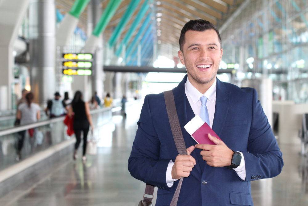 Smiling traveller in suit holding passport and boarding pass inside bright, modern airport terminal