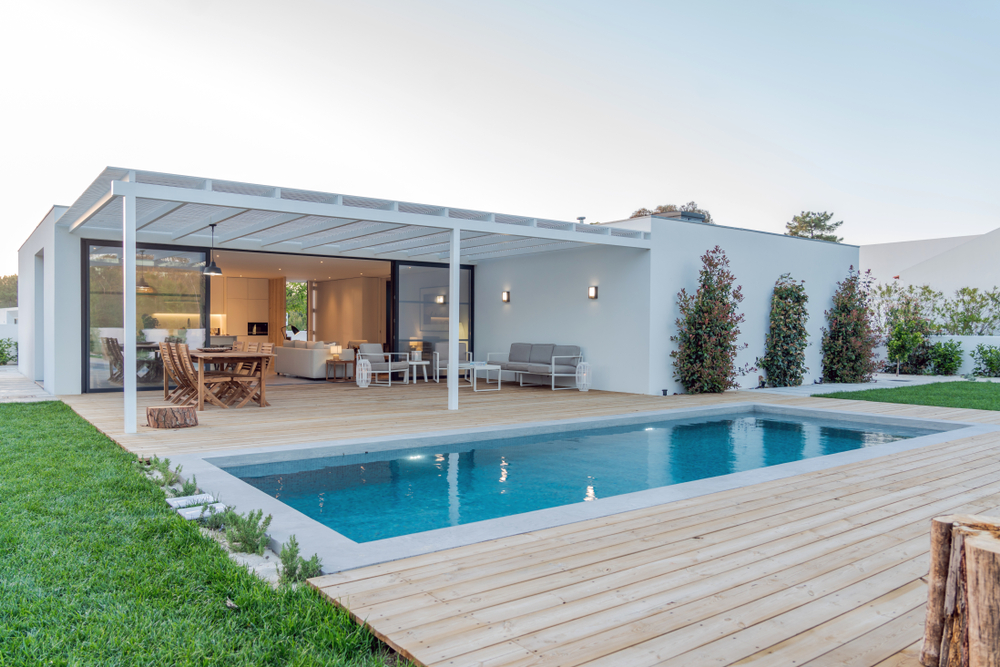 Modern white villa with a pool and wooden deck featuring an outdoor lounge and dining area