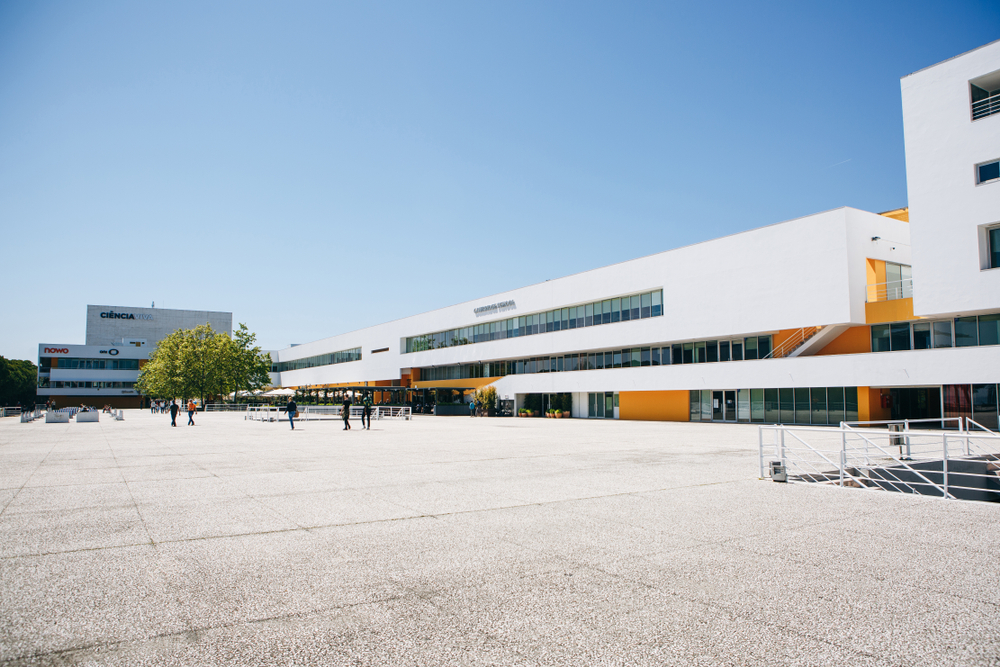 Modern, elongated white and orange school building facing a vast, open concrete plaza
