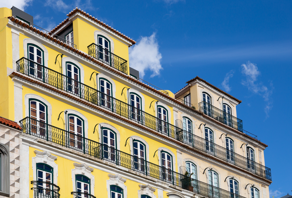 Portuguese-style vintage house with bright yellow and white facade, tall windows and long balconies