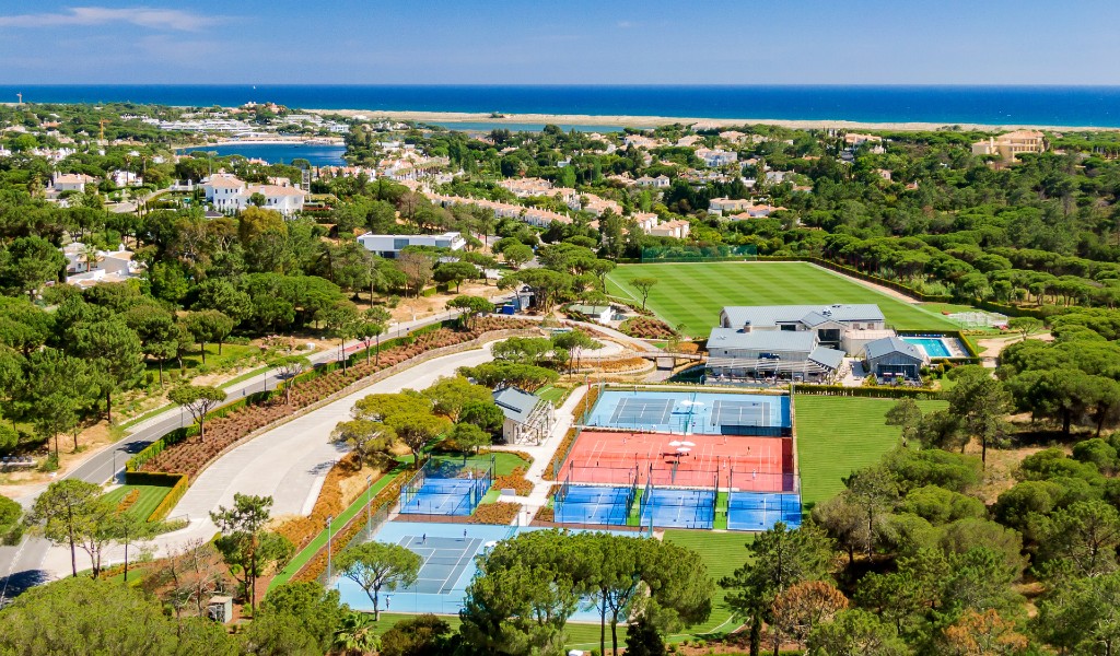 Aerial view of a luxury sports complex with tennis courts, soccer field, and pool
