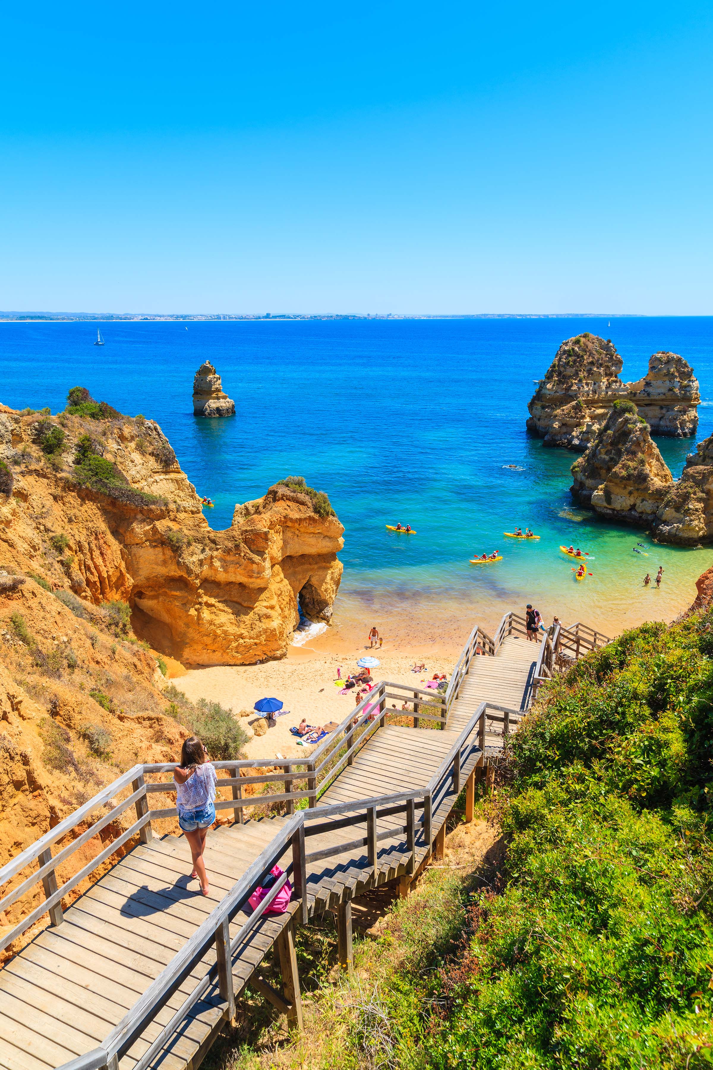 Young woman on wooden steps leading down to sunny Praia do Camilo beach