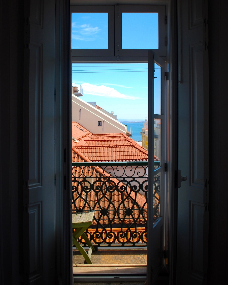 View from a balcony with ornate railing overlooking red-tiled rooftops and blue ocean