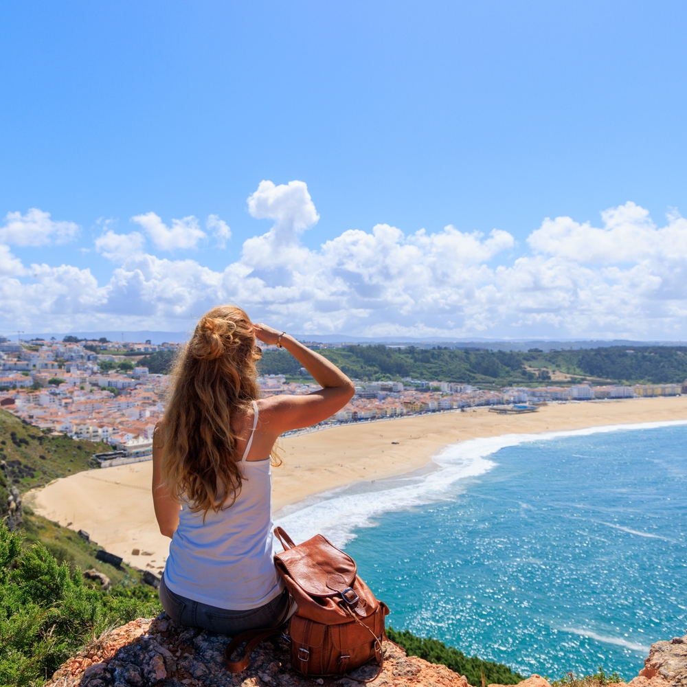 Woman overlooking panoramic view of beautiful beach and turquoise sea in Nazare, Portugal