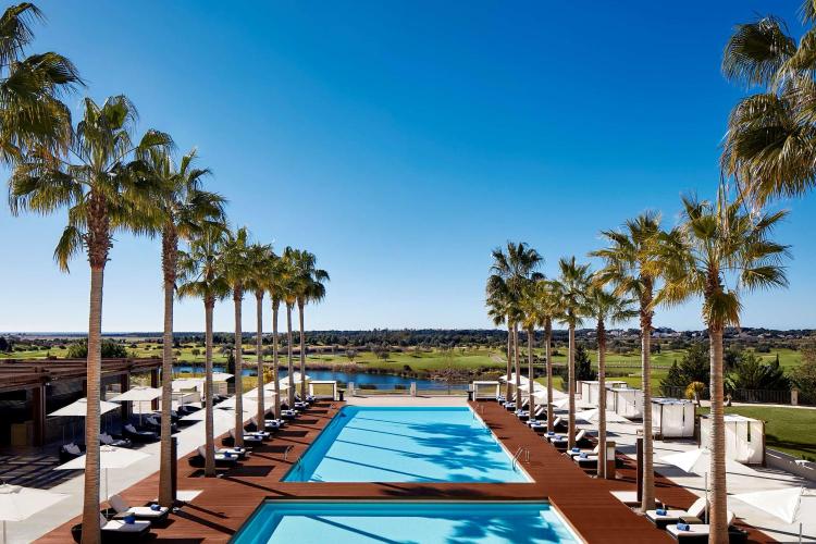 Luxury resort swimming pool with a wooden deck, palm trees and golf course view