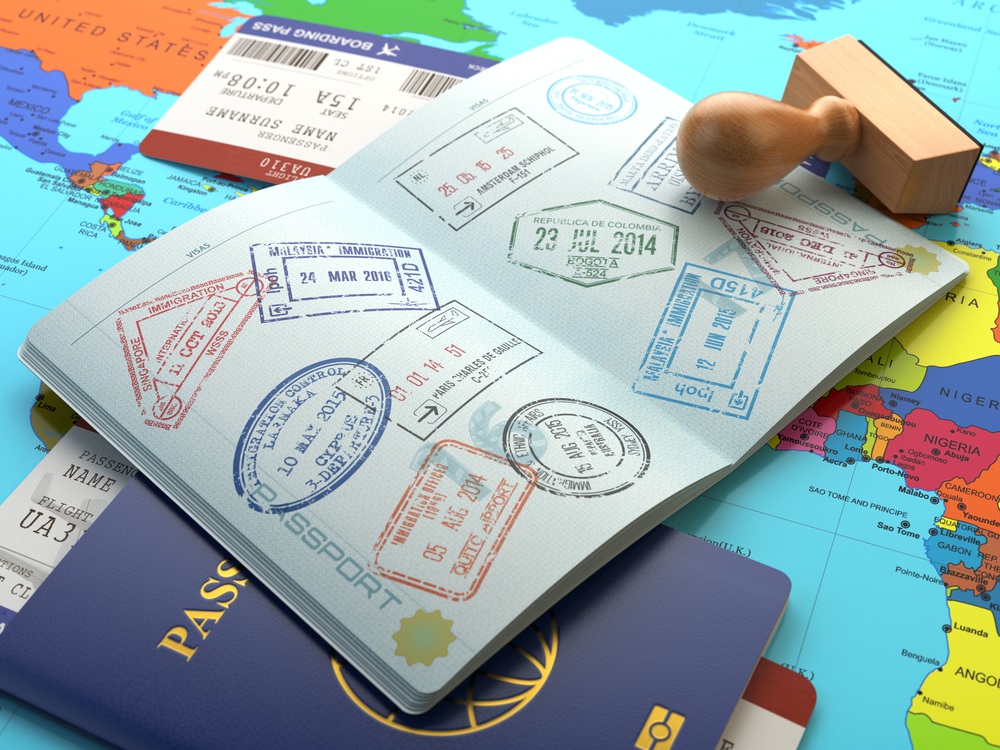 An open passport with many colorful entry stamps rests on a world map with a wooden stamper