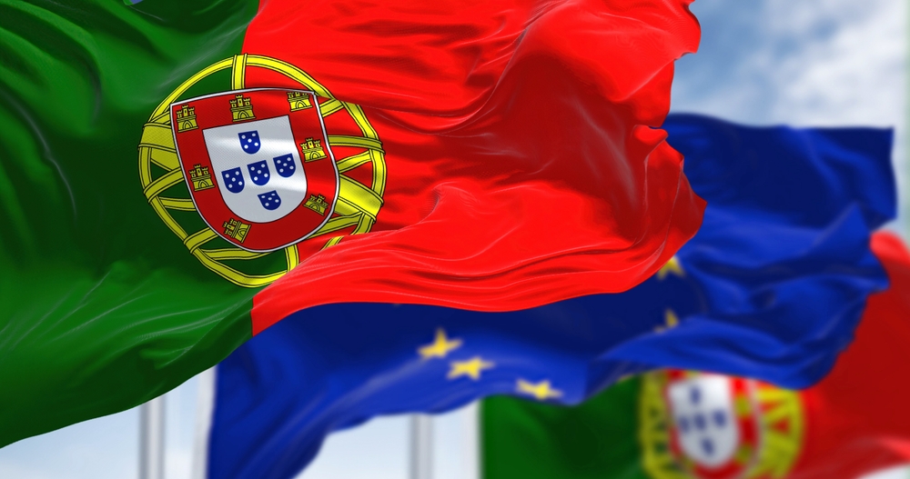 The Portuguese and European Union flags wave together against a bright, slightly cloudy sky