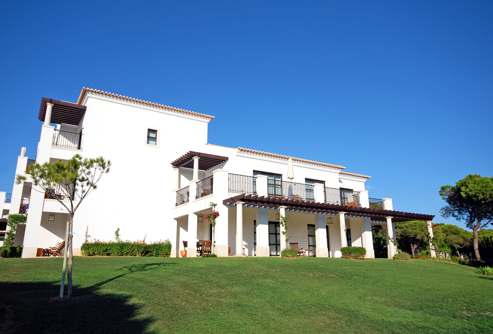 Luxury white villa with multiple balconies and a green lawn under a clear blue sky
