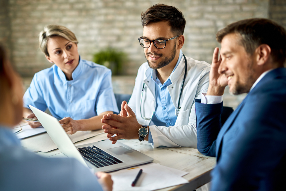Doctor in white coat and glasses discusses medical data on a laptop with colleagues