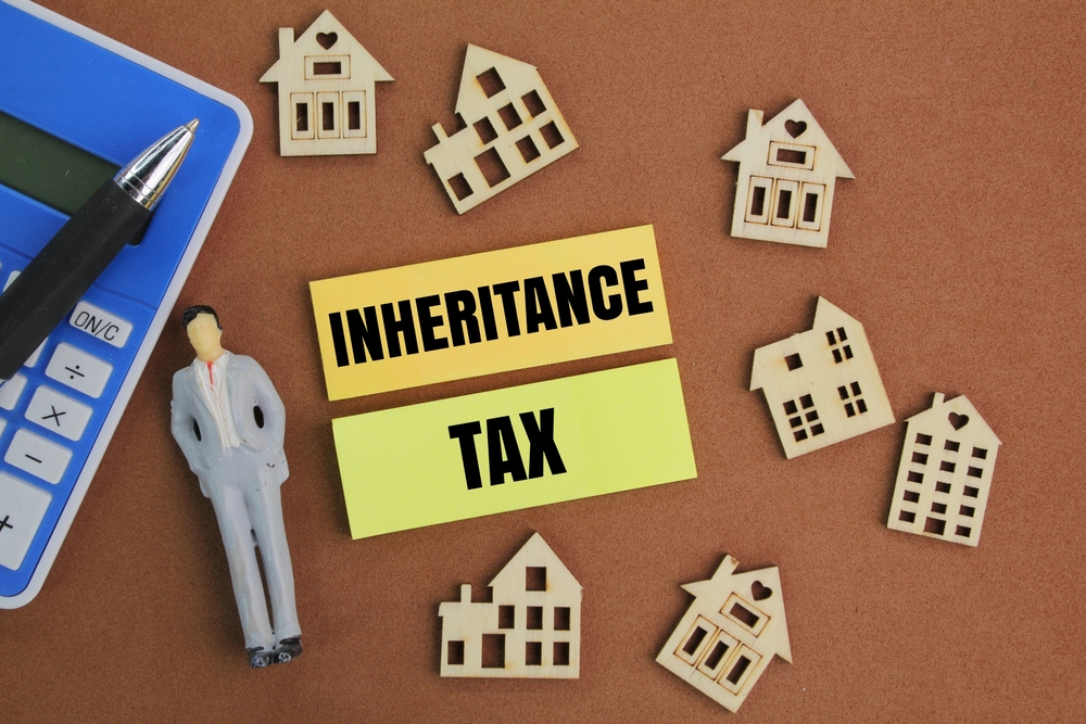 Top-down view of a calculator, small wooden houses and 'Inheritance Tax' signs on a desk