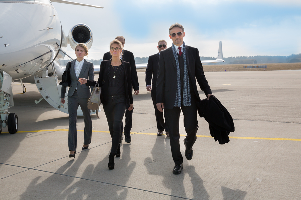 Group of business professionals in suits walking across a sunny tarmac from a private jet