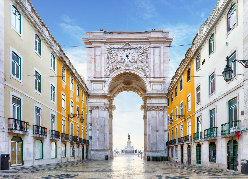 The Rua Augusta Arch, in Lisbon, stands between yellow buildings at the end of a cobblestone street