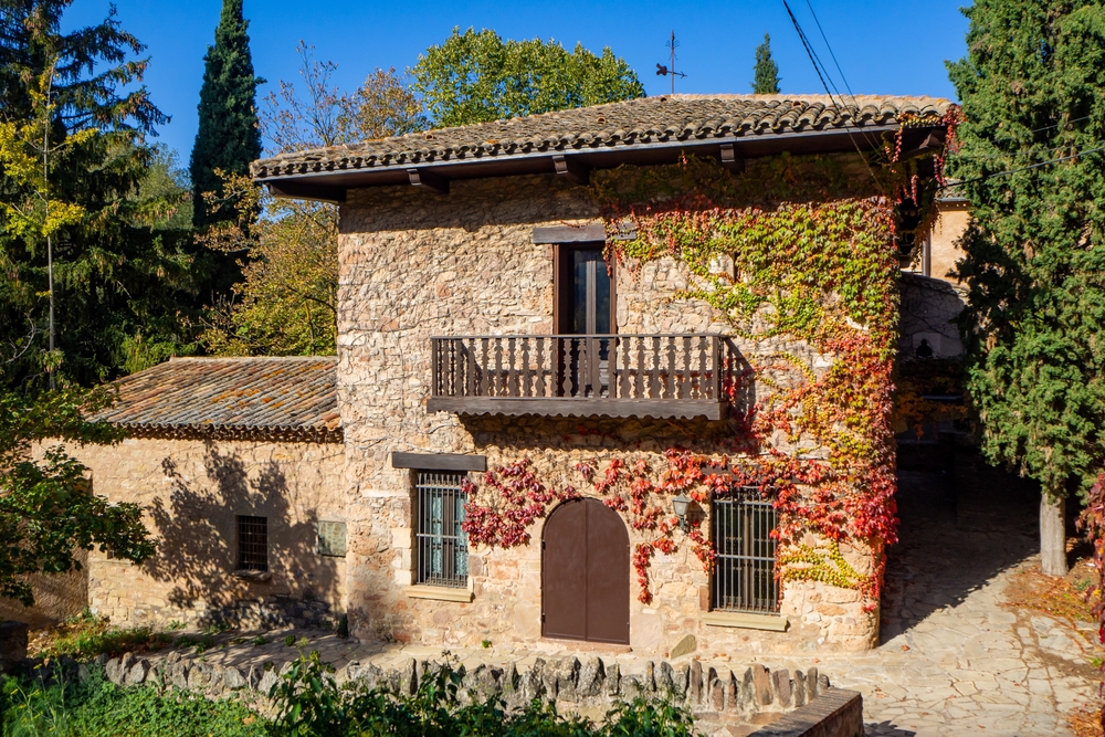 Rustic Mediterranean stone house with ivy-covered walls, tiled roof and arched doorway in countryside