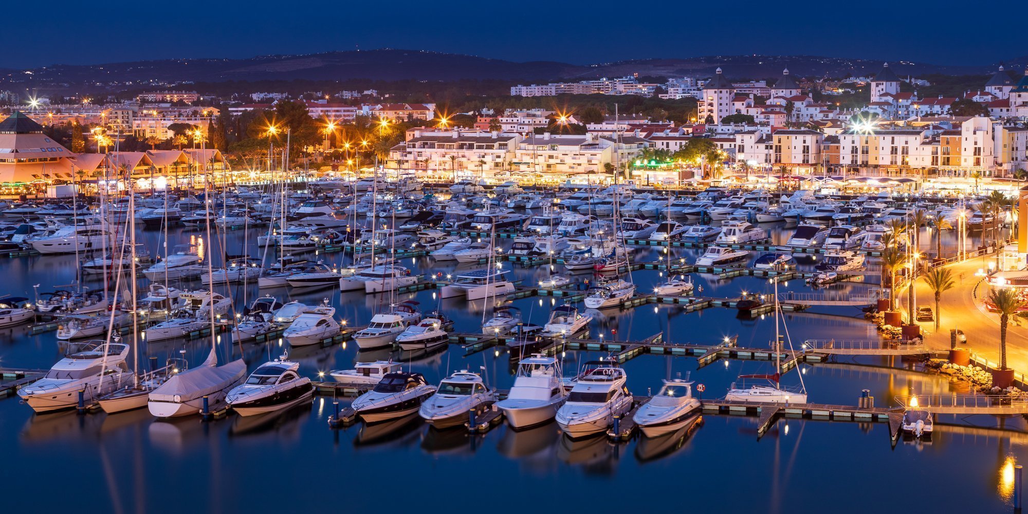 Vilamoura marina at night with yachts, glowing waterfront lights and hillside town in the background